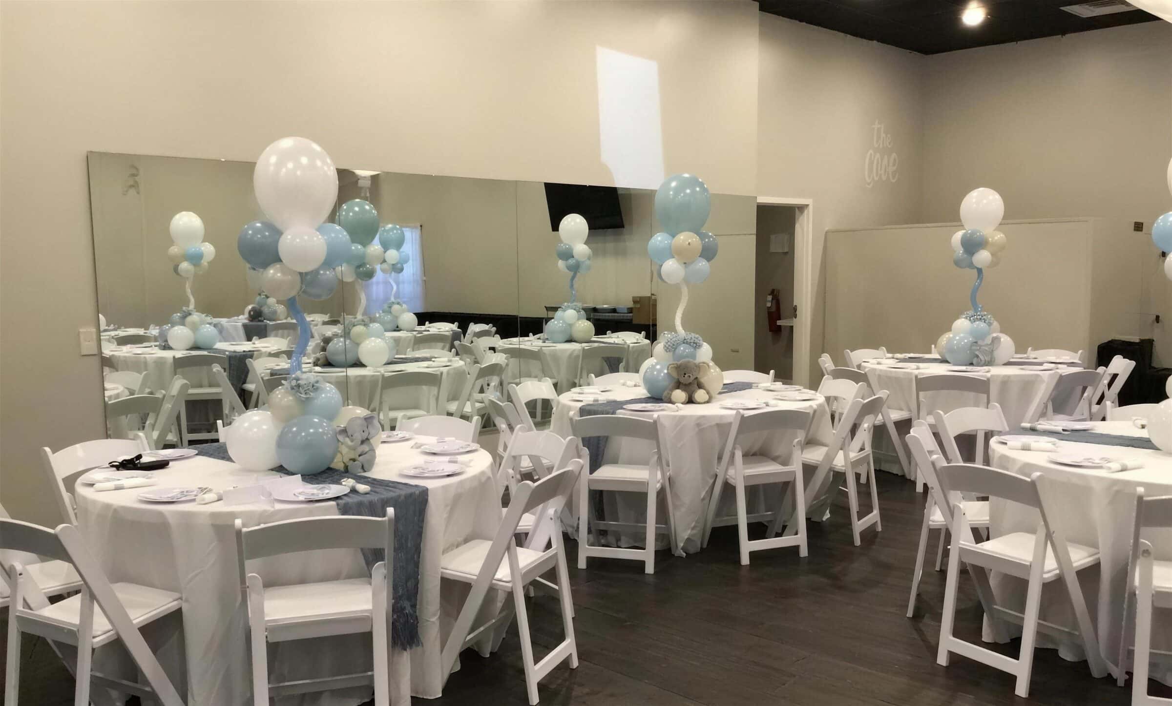 Round guest tables in white linens with gray runners and tall blue-and-white balloon centerpieces topped with elephant plush at a baby shower at The Cove at St. Johns, St. Johns County FL