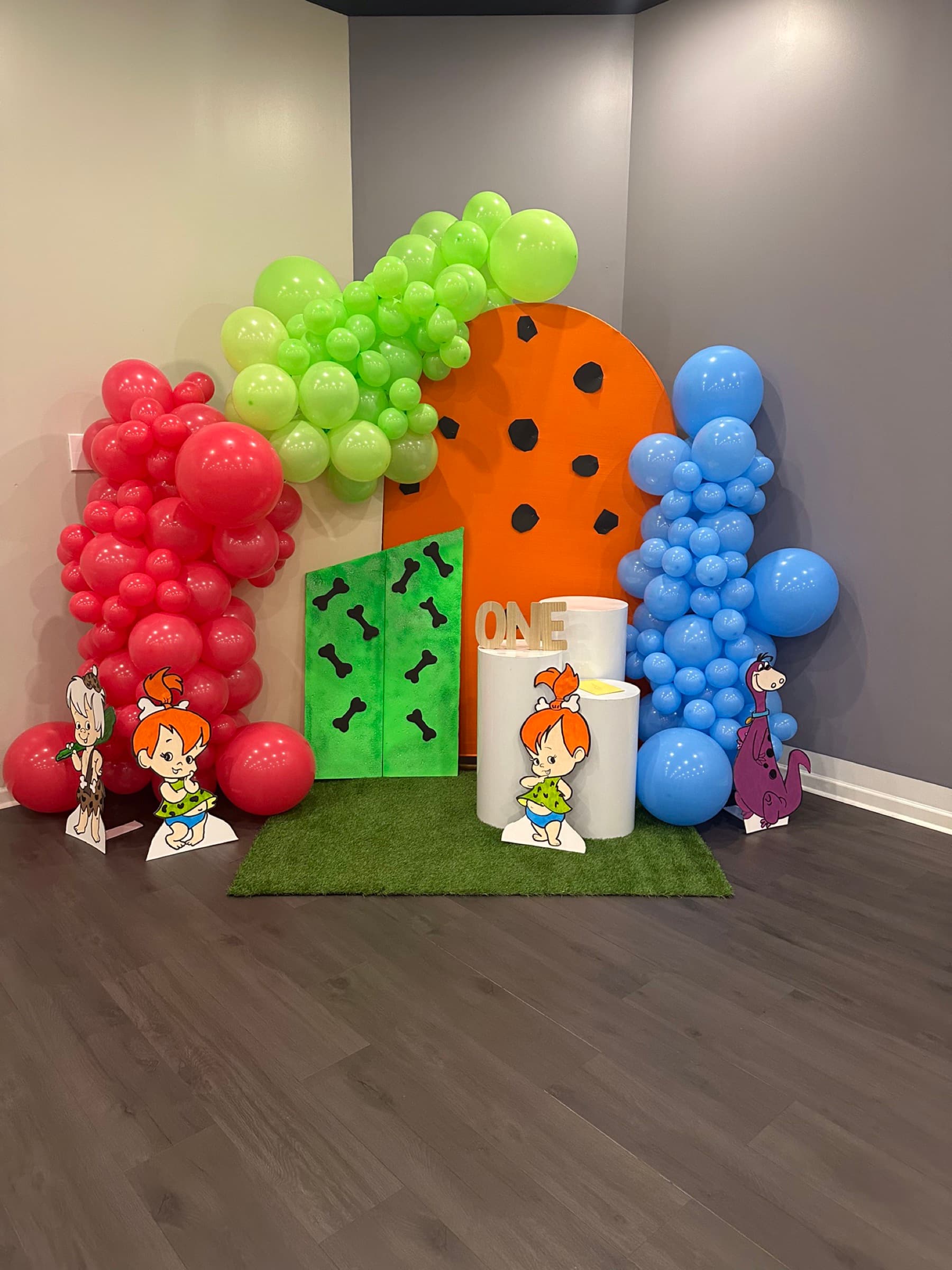 First birthday party backdrop with colorful balloon garlands and cartoon character cutouts, styled in-house at The Cove at St. Johns, Fruit Cove FL