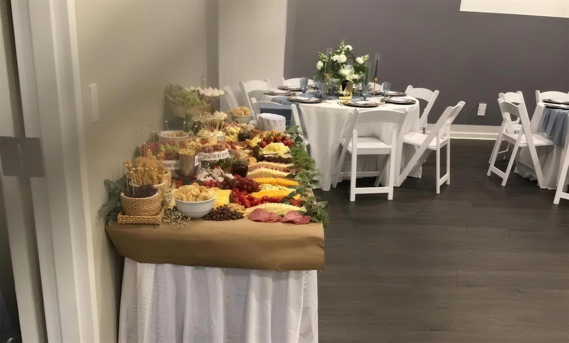 Grazing table of sliced meats, cheeses, grapes and crackers on kraft paper with eucalyptus, next to a dusty-blue and gold round table at The Cove at St. Johns, near Jacksonville, FL