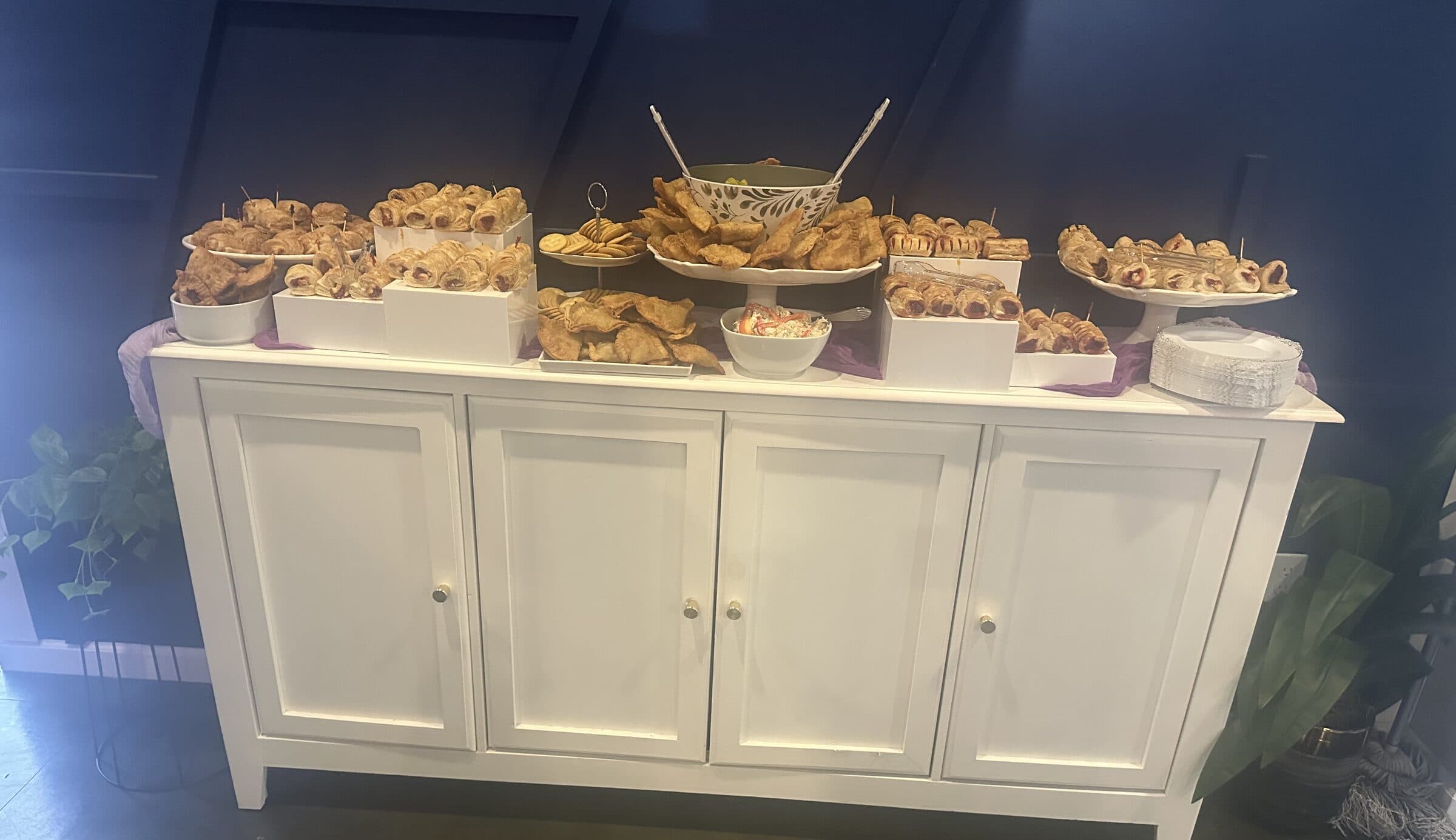 Savory buffet on a white credenza with empanadas, pastelitos, pigs in blankets, crackers and a bowl of dip over lavender cheesecloth at The Cove at St. Johns, St. Johns County FL