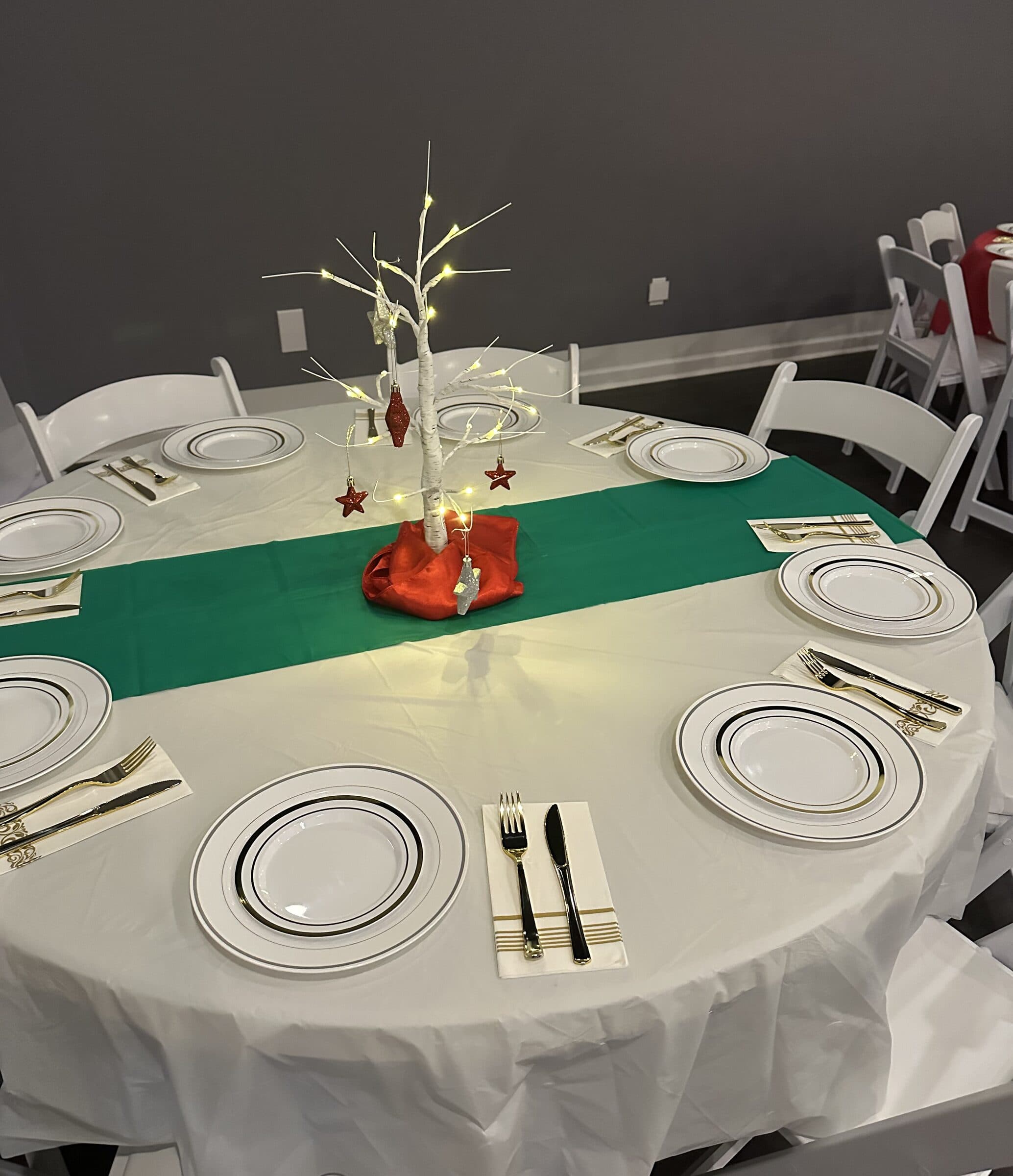 Holiday place settings of gold-rim plates and gold flatware around a lit white birch twig centerpiece with red star ornaments on a green runner at The Cove at St. Johns, St. Johns County FL