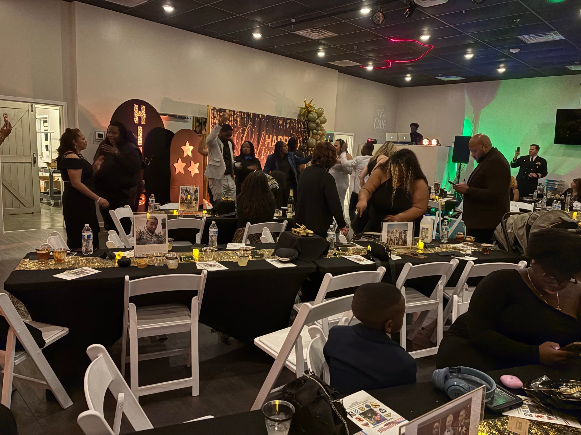 Guests gathered at a celebration with black linens, gold sequin runners and a lit marquee backdrop at The Cove at St. Johns in Fruit Cove, FL
