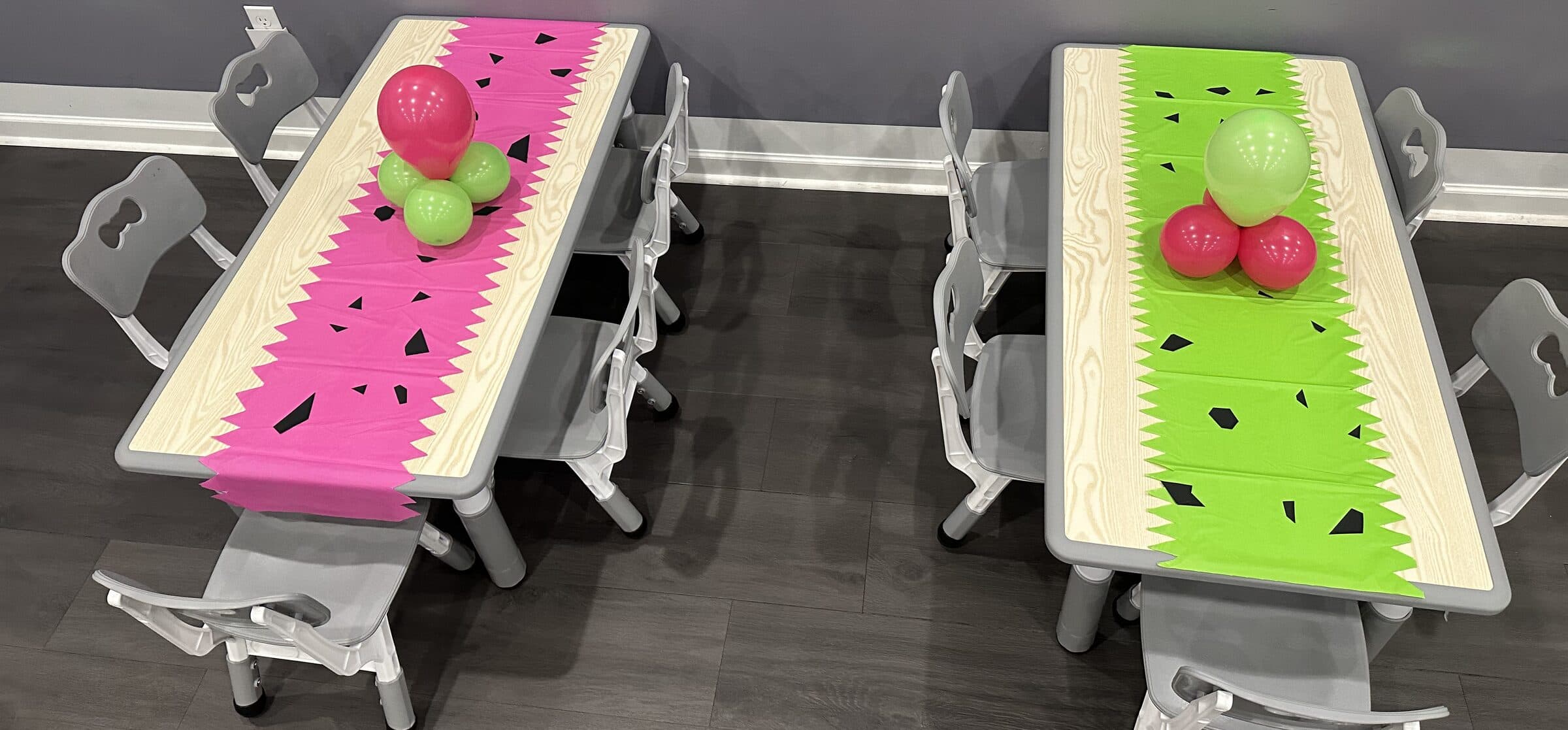 Two kids' tables dressed as watermelon slices in pink and green paper runners with balloon clusters at a children's birthday at The Cove at St. Johns, St. Johns County FL