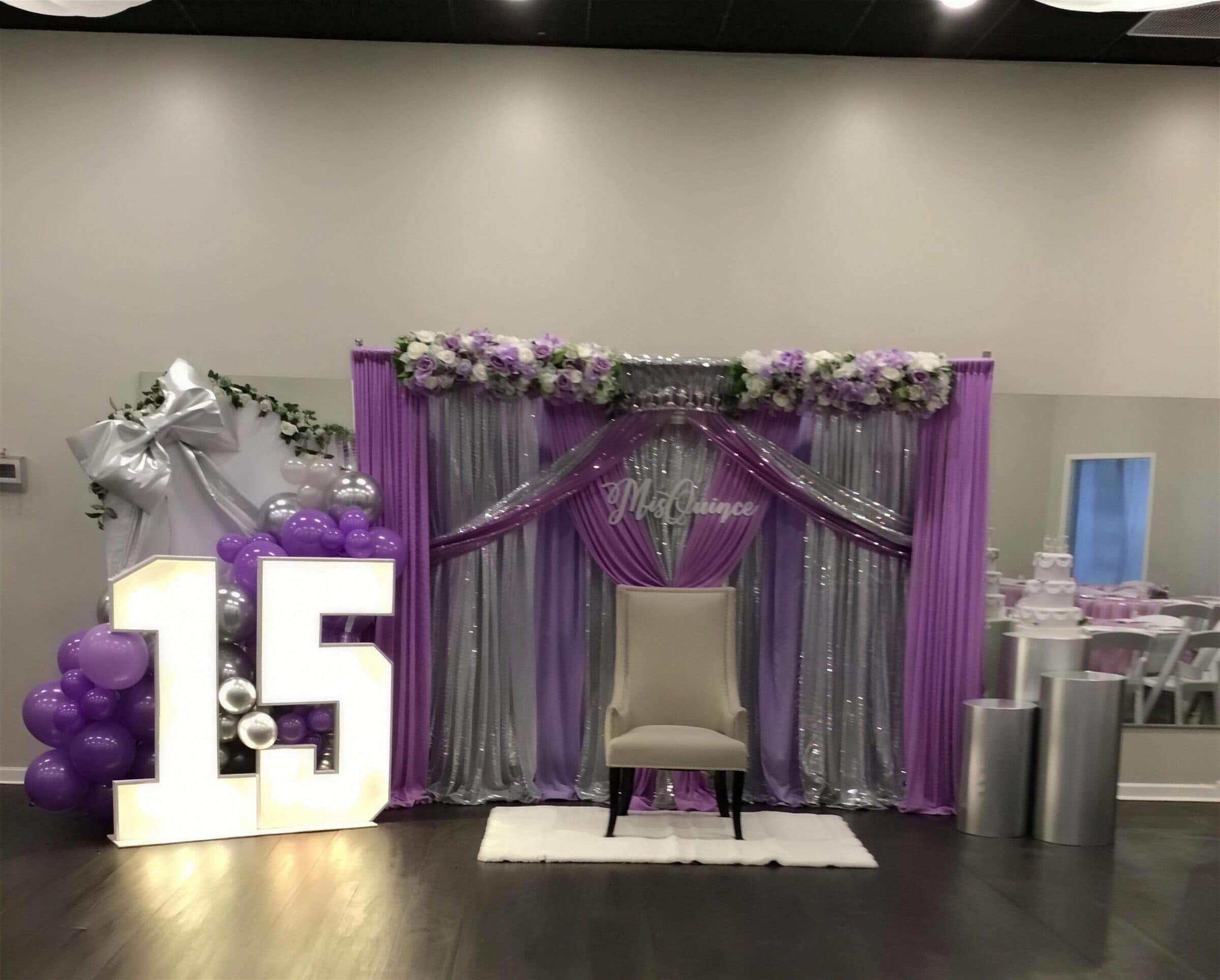 Purple and silver Mis Quince backdrop with a lavender floral swag, throne chair and glowing marquee 15 at The Cove at St. Johns, St. Johns County FL