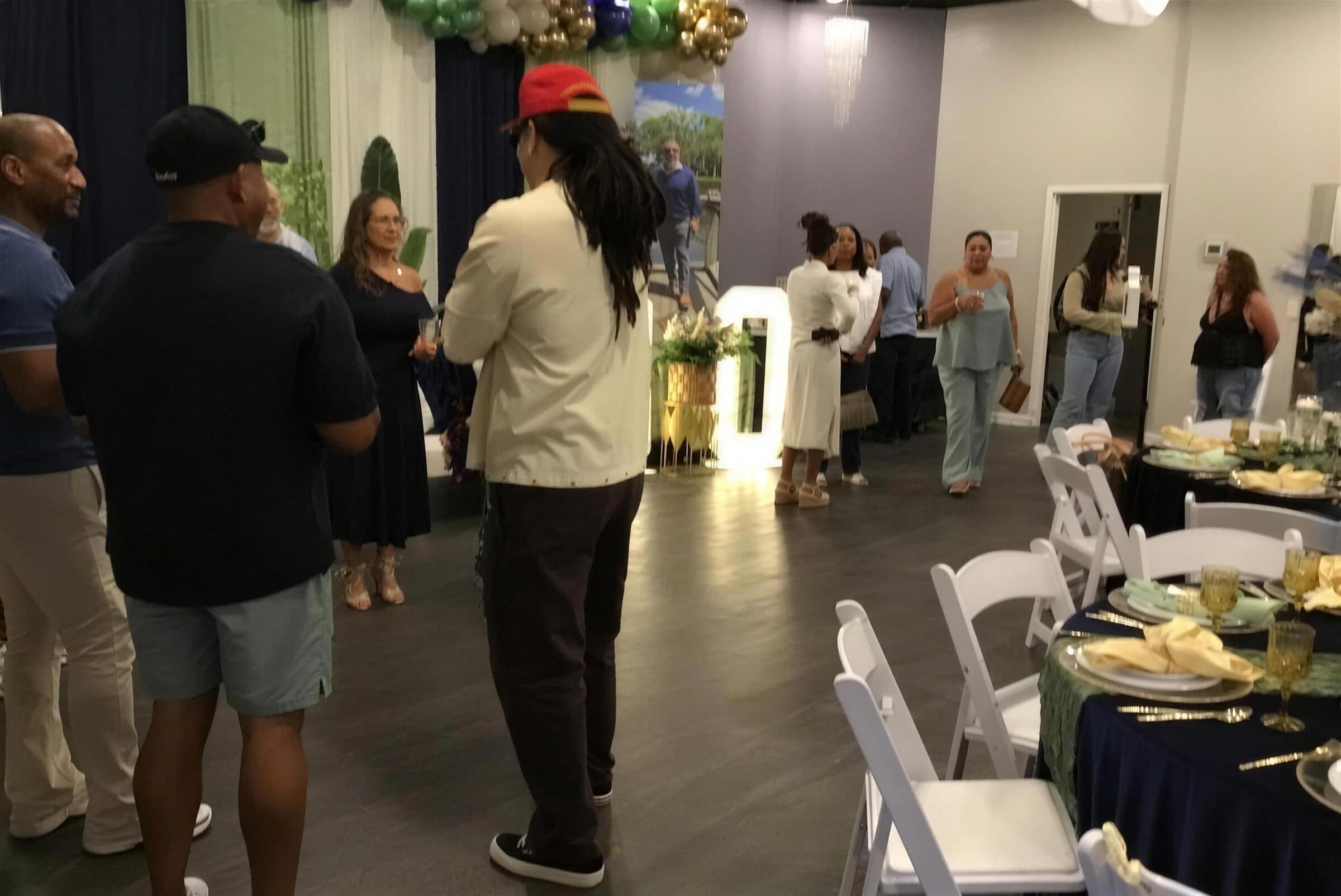 Guests mingling near a lit marquee number and green, navy and gold balloon garland at a milestone birthday at The Cove at St. Johns, Fruit Cove FL