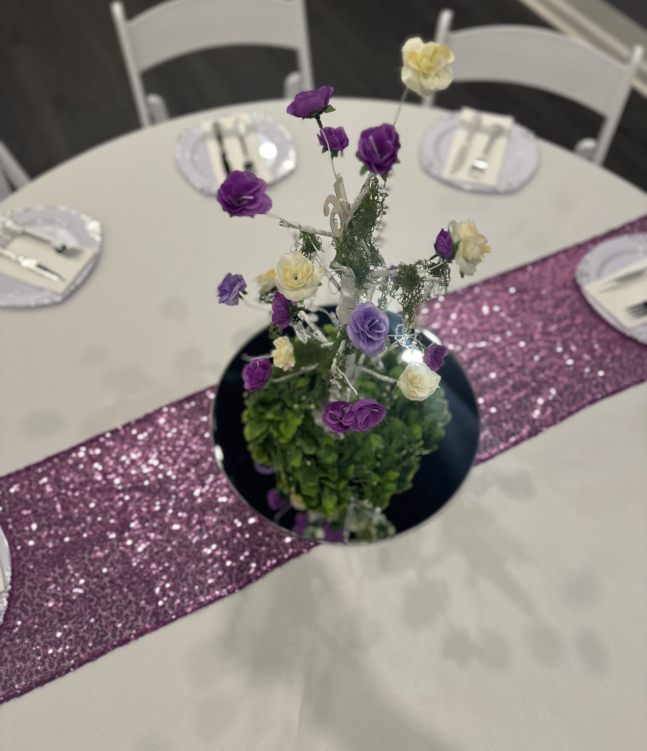Overhead look at a purple and cream silk rose centerpiece on a mirrored base with a pink sequin runner at The Cove at St. Johns, Fruit Cove, St. Johns County FL