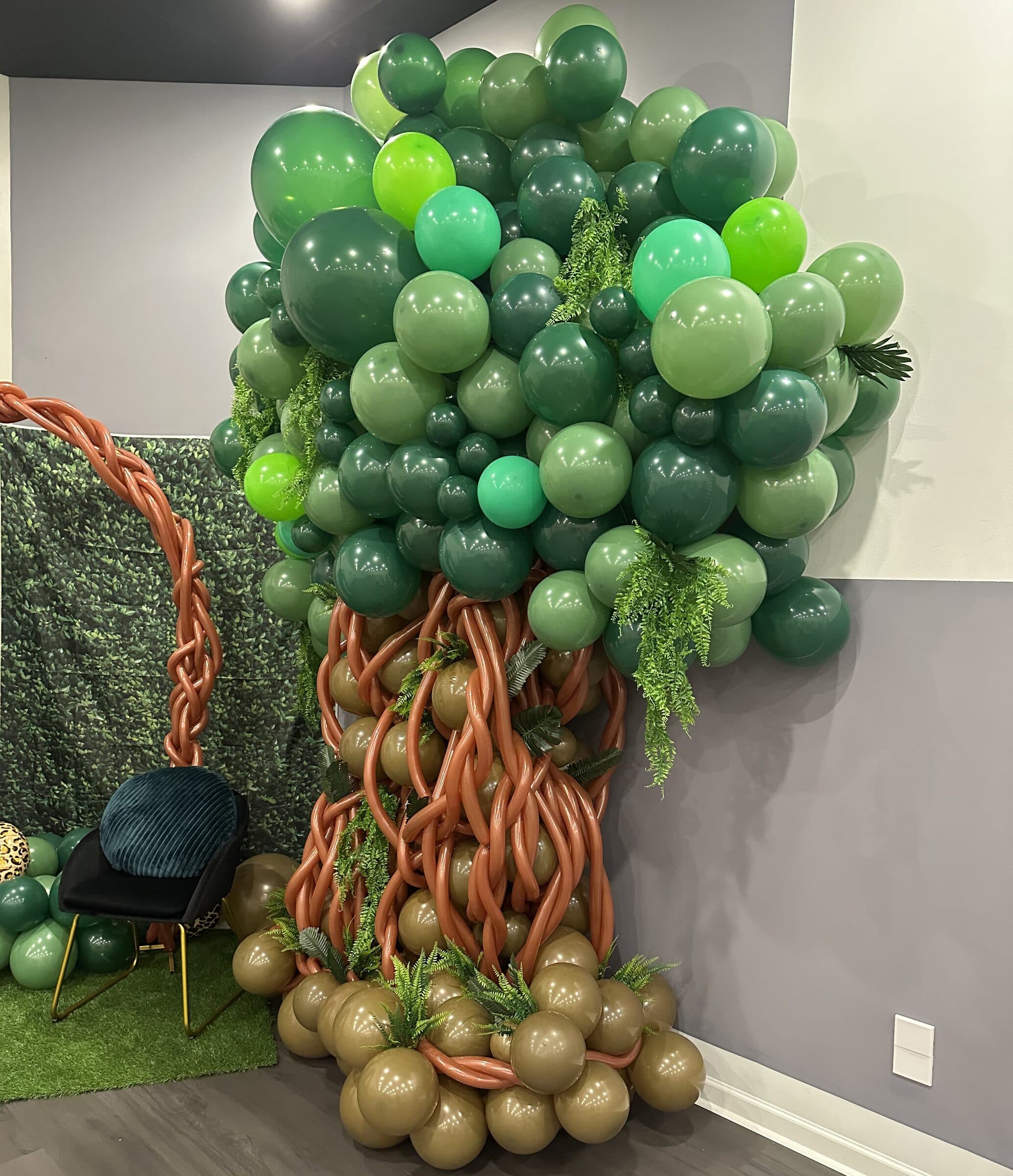 Jungle-tree balloon sculpture in layered greens with a braided trunk, hanging ferns and a boxwood wall at a birthday party at The Cove at St. Johns, Fruit Cove FL