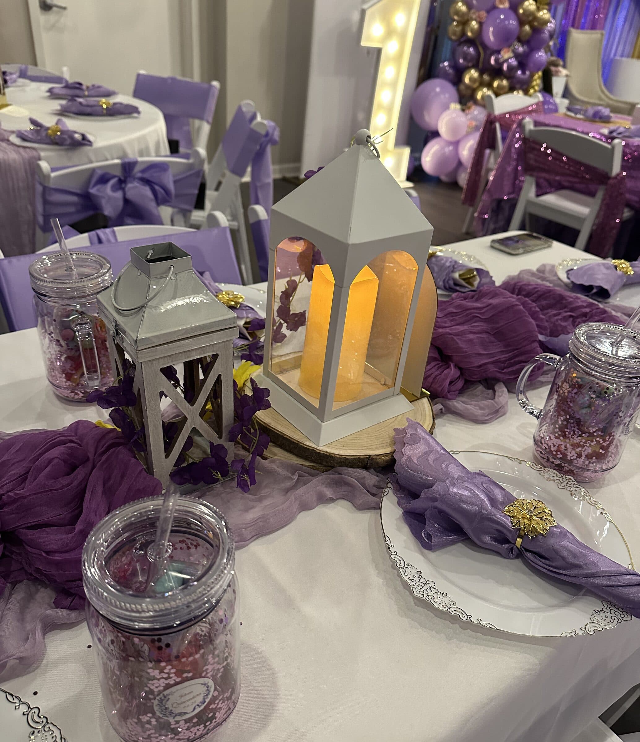 Quinceanera table close-up - white lantern on a wood slice, plum cheesecloth runner, glitter mason jar favors and lavender napkins at The Cove at St. Johns, Fruit Cove FL
