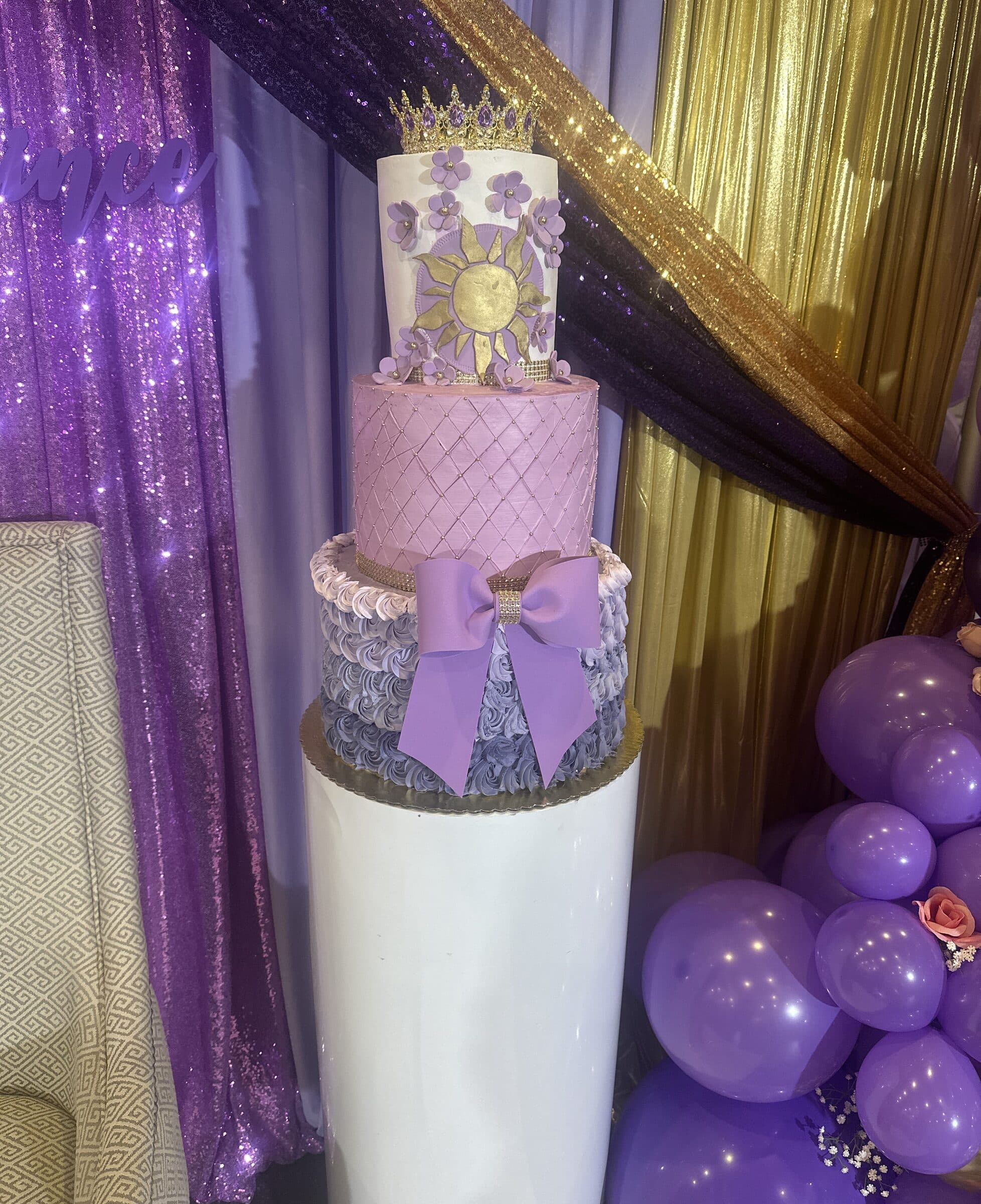 Three-tier lavender quinceanera cake with a gold sun medallion, sugar flowers, a purple bow and a jeweled crown topper at The Cove at St. Johns, Fruit Cove FL