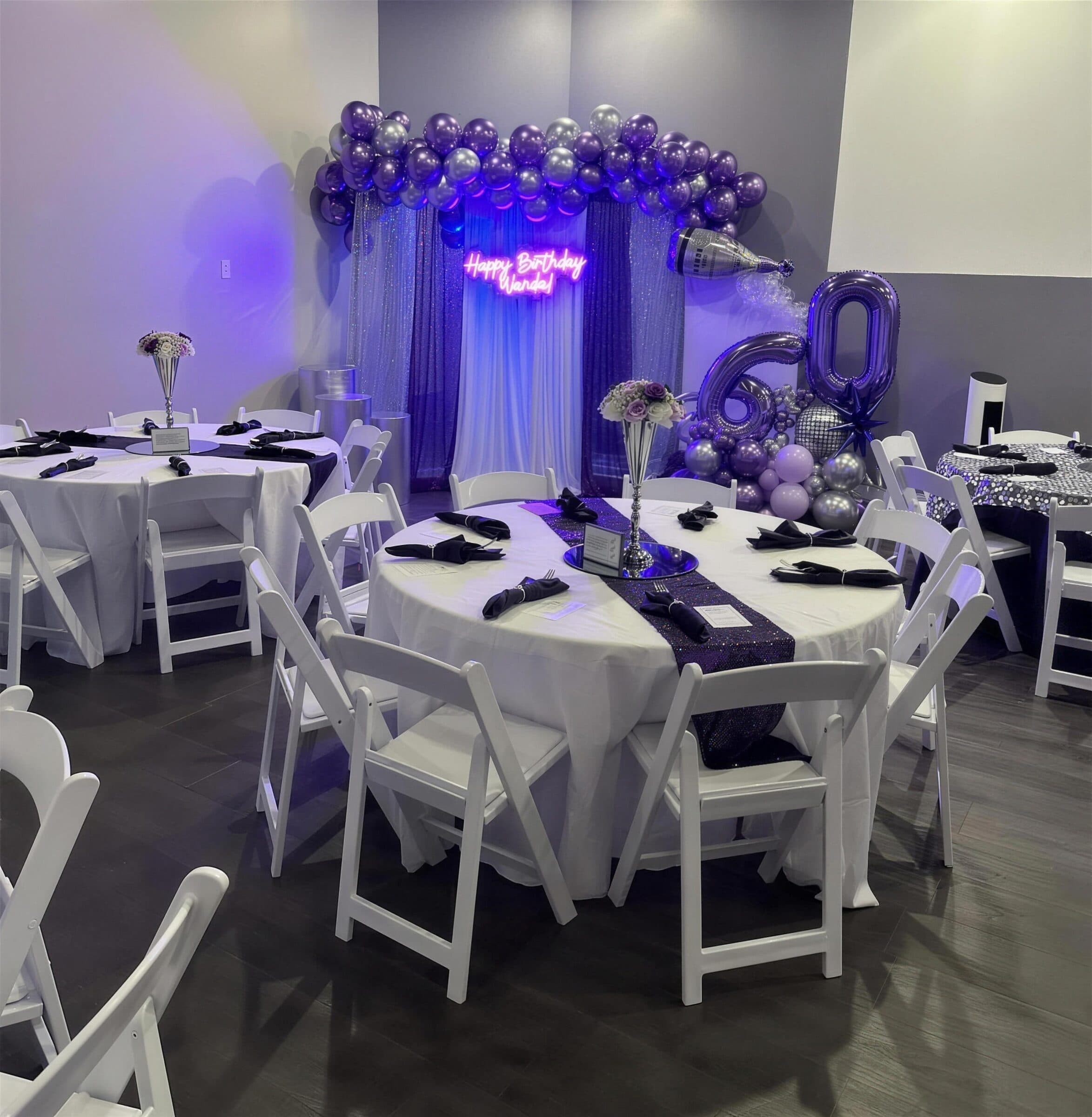Purple and silver 60th birthday reception with white rounds, sequin runners, black napkins, a neon birthday sign and giant 60 number balloons at The Cove at St. Johns, St. Johns County FL
