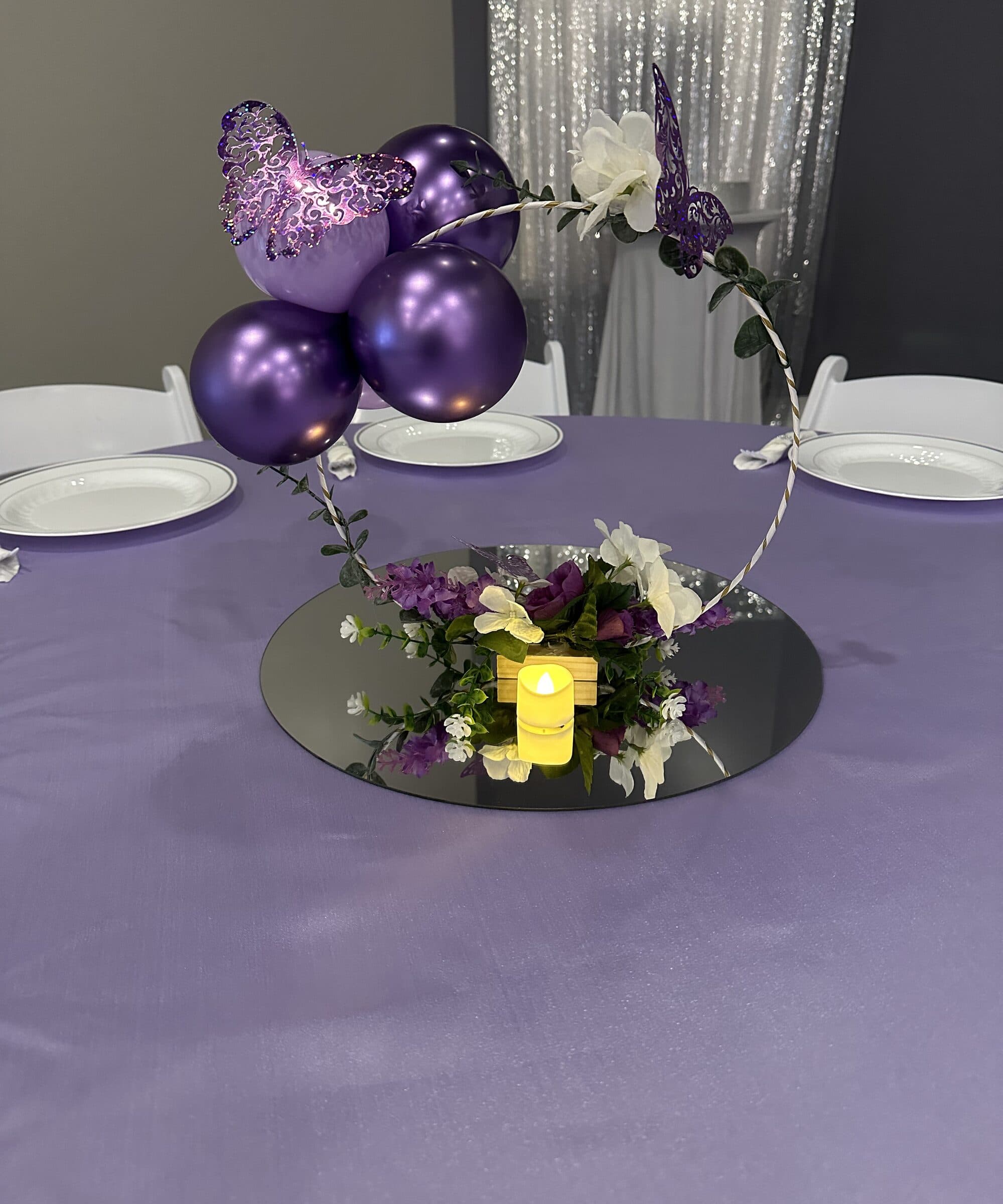 Butterfly hoop centerpiece on a round mirror with silk florals and a flameless candle, on lavender linen at a Sweet 16 at The Cove at St. Johns, Fruit Cove FL