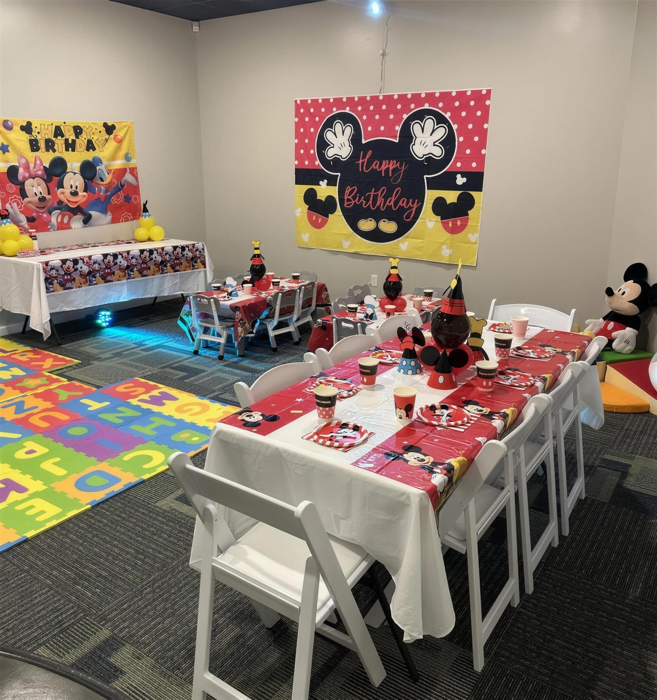 Kids' birthday room with red cartoon-print table covers, party hats, a foam alphabet play mat and matching character backdrops at The Cove at St. Johns, near Jacksonville, FL