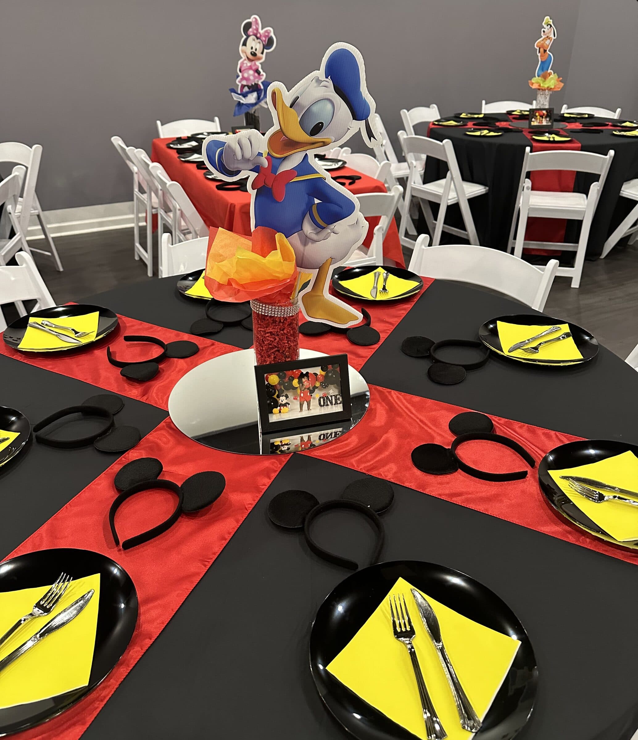 Mickey Mouse table setting at The Cove at St. Johns, St. Johns County FL - black linen, red satin cross runners, black plates with yellow napkins and mouse-ear headbands