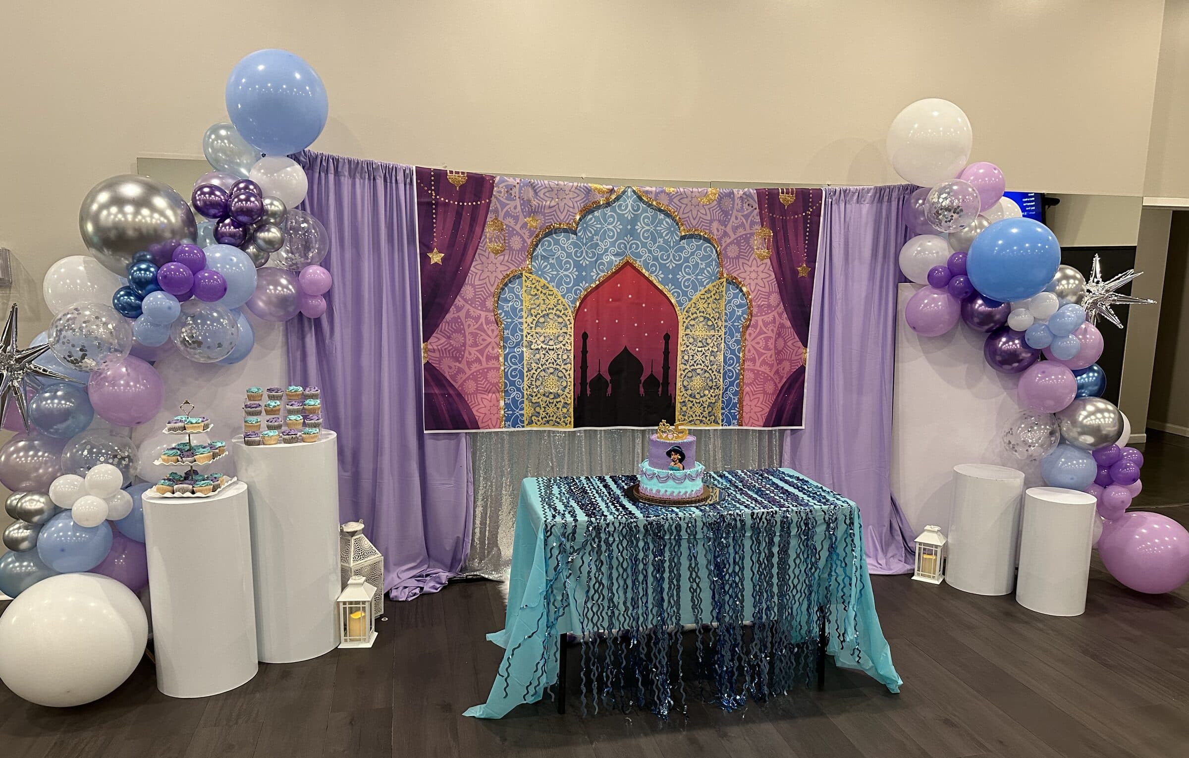 Princess-themed cake table with a palace backdrop, lavender draping, purple and silver balloon arches, cupcake pedestals and a turquoise fringe cloth at The Cove at St. Johns, Fruit Cove FL