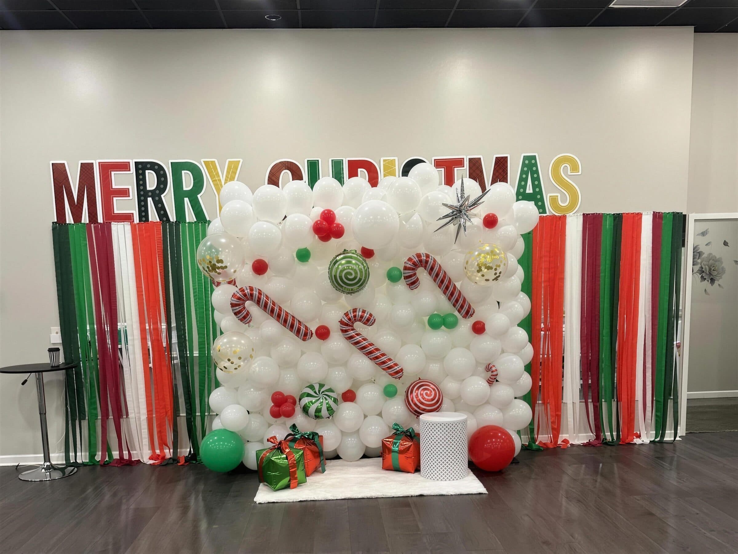 Merry Christmas balloon wall in white with candy cane and peppermint foils, red and green streamer curtains and wrapped gifts at The Cove at St. Johns, St. Johns County FL