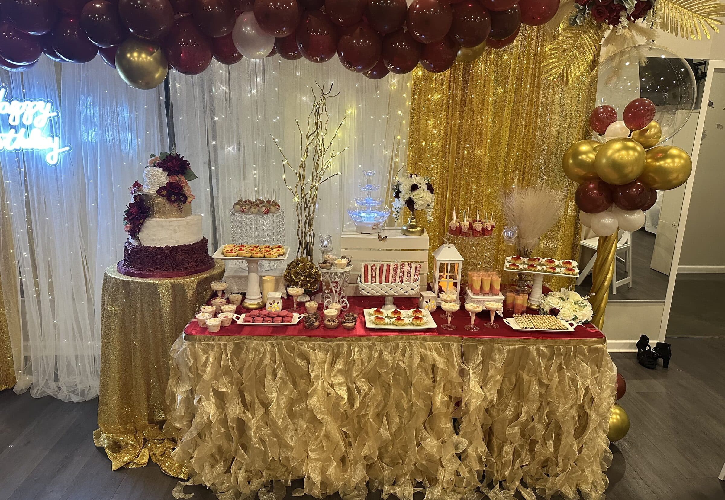Close view of the same burgundy and gold dessert table - macarons, cake pops, a chocolate fountain, lanterns and a gold ruffle skirt at The Cove at St. Johns, near Jacksonville, FL