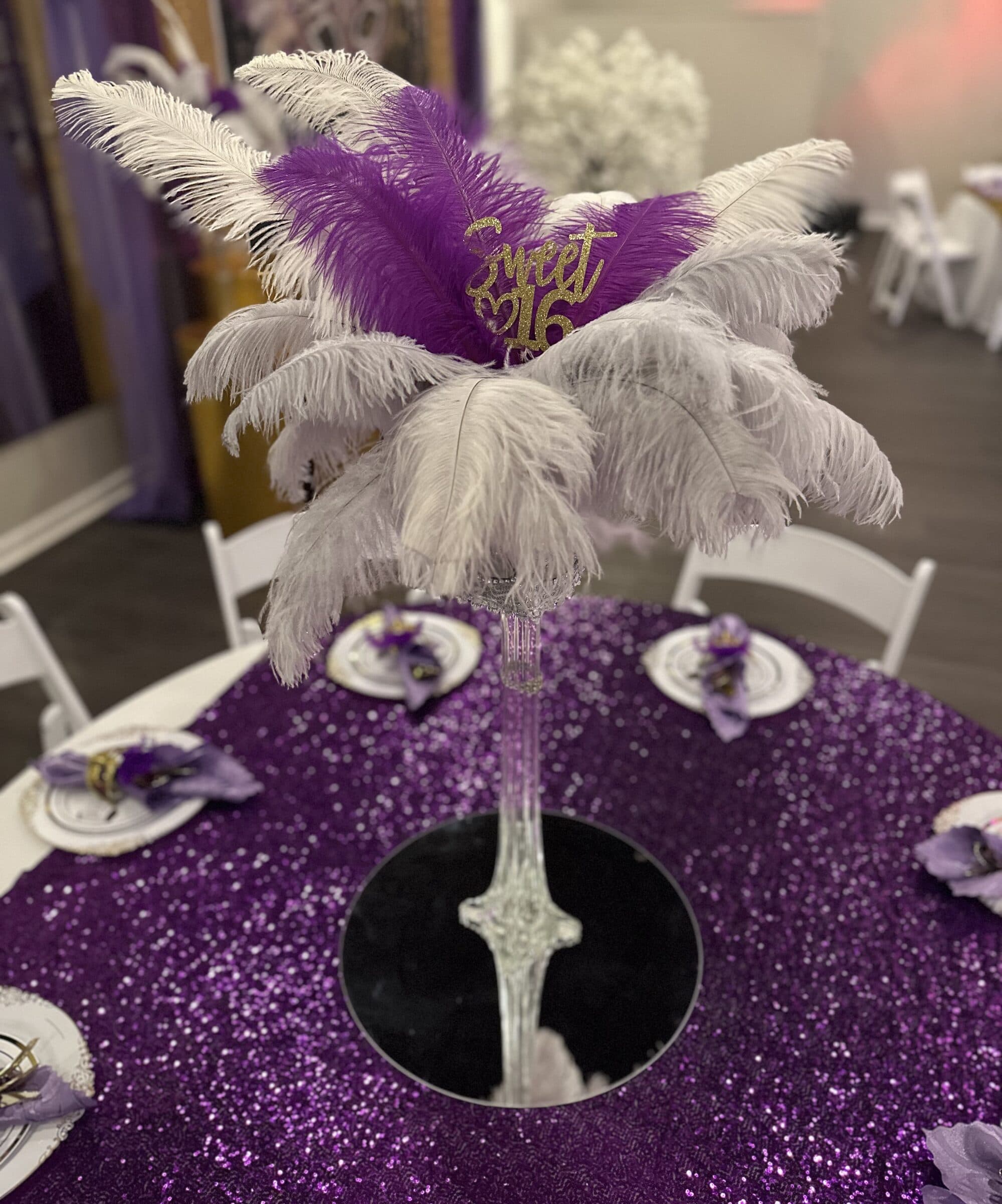 Tall ostrich feather centerpiece with a gold Sweet 16 topper on a purple sequin tablecloth with mirror base and lilac napkins at The Cove at St. Johns, Fruit Cove FL