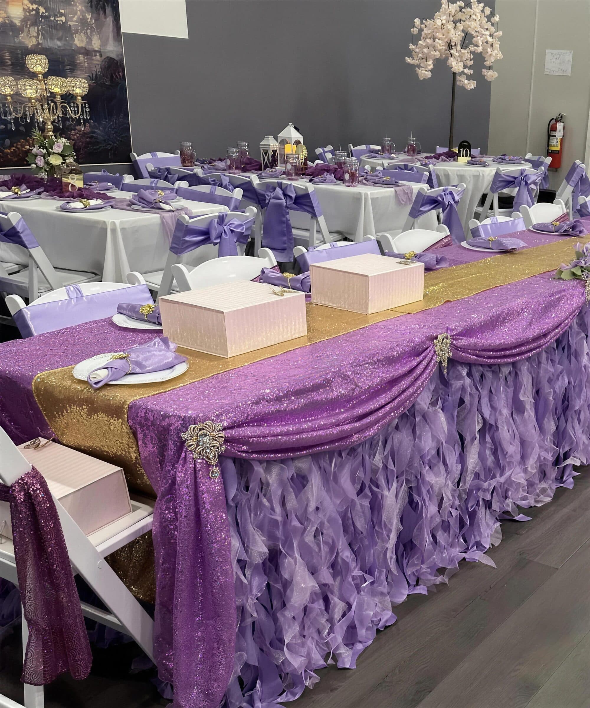 Quinceanera head table at The Cove at St. Johns, Fruit Cove, St. Johns County FL - purple sequin swag over a gold runner, lilac curly-willow skirt, brooches and lavender chair sashes beyond