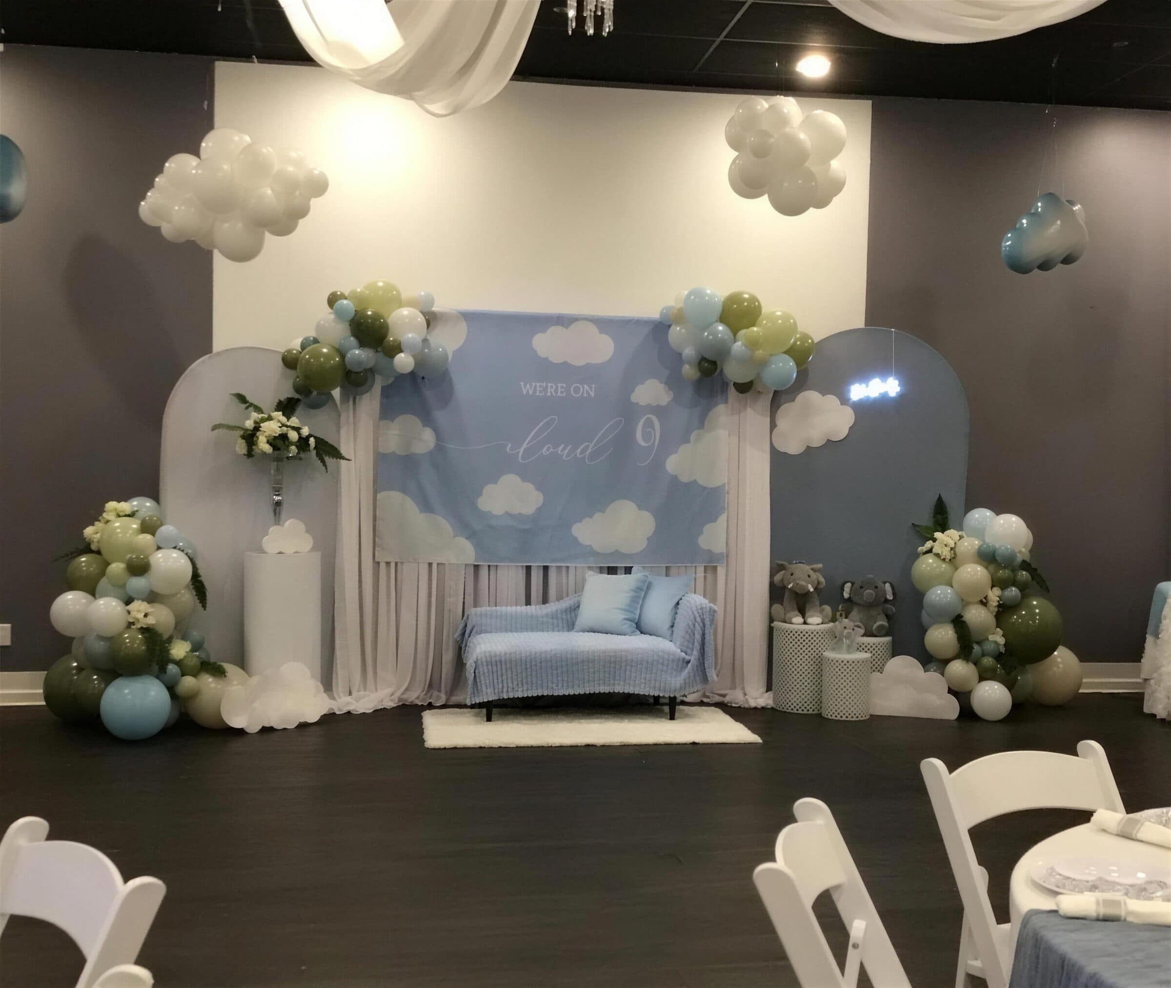 Room-level view of the cloud-themed lounge with ceiling draping, arch panels and elephant plush beside guest tables, baby shower at The Cove at St. Johns, Fruit Cove, St. Johns County FL