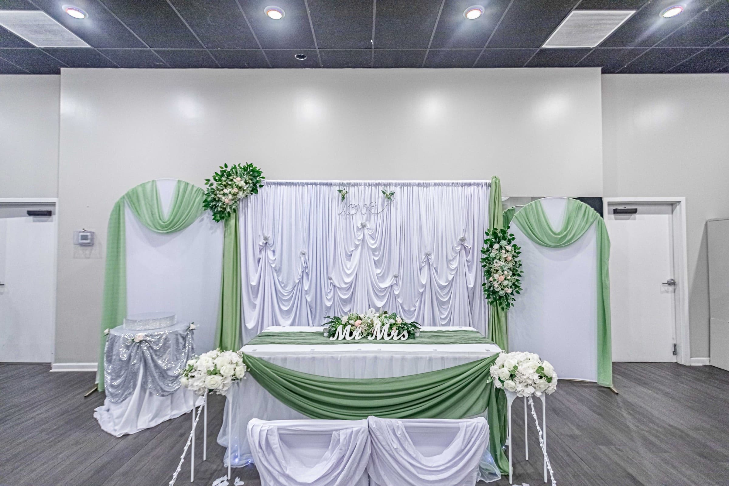 A sage and white head-table backdrop with chiffon draping and florals, styled in-house at The Cove at St. Johns in Fruit Cove, FL
