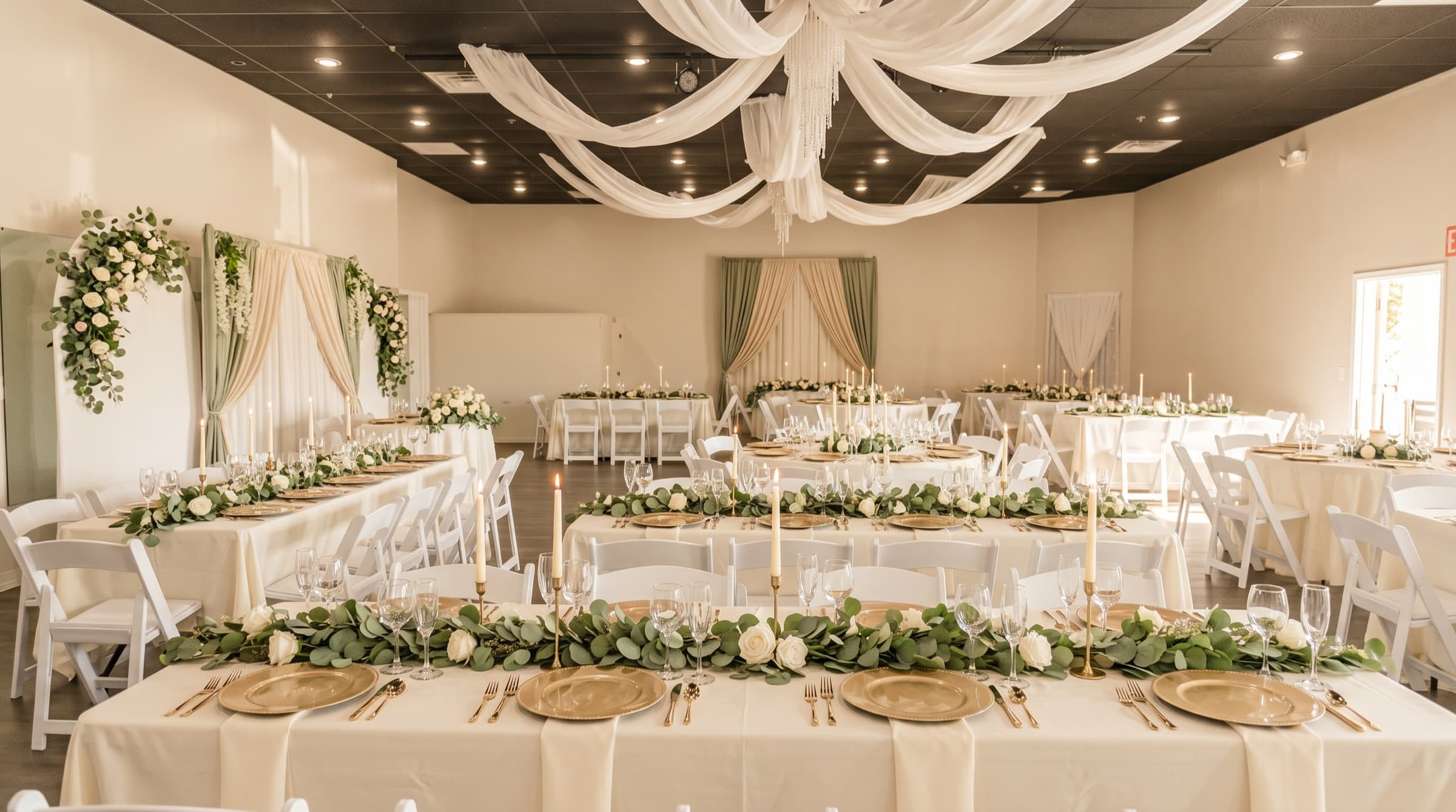 Wedding reception hall with draped ceiling, greenery runners, and gold place settings at The Cove at St. Johns in Fruit Cove, FL
