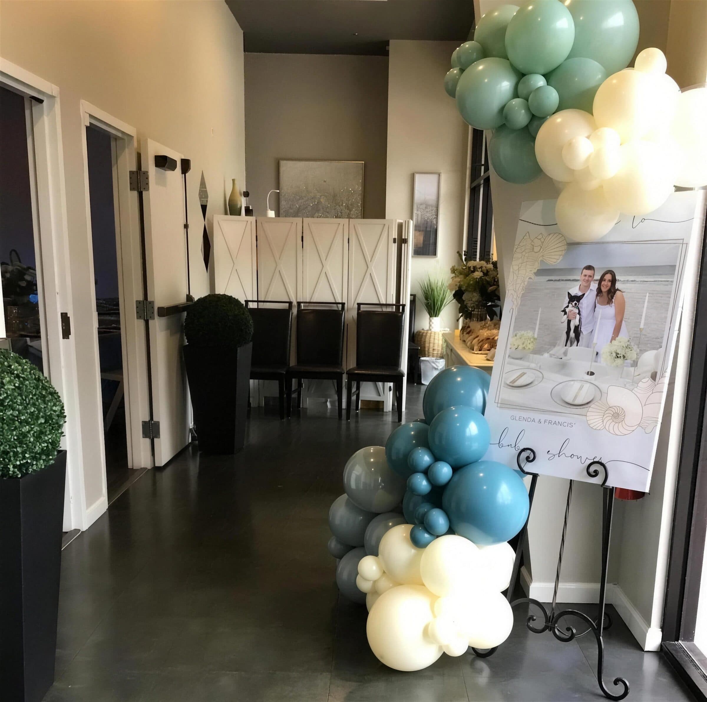 Entry lounge dressed for a baby shower at The Cove at St. Johns - sage, cream and dusty-blue balloon garlands, a framed welcome sign on a scroll easel and boxwood topiaries, Fruit Cove FL