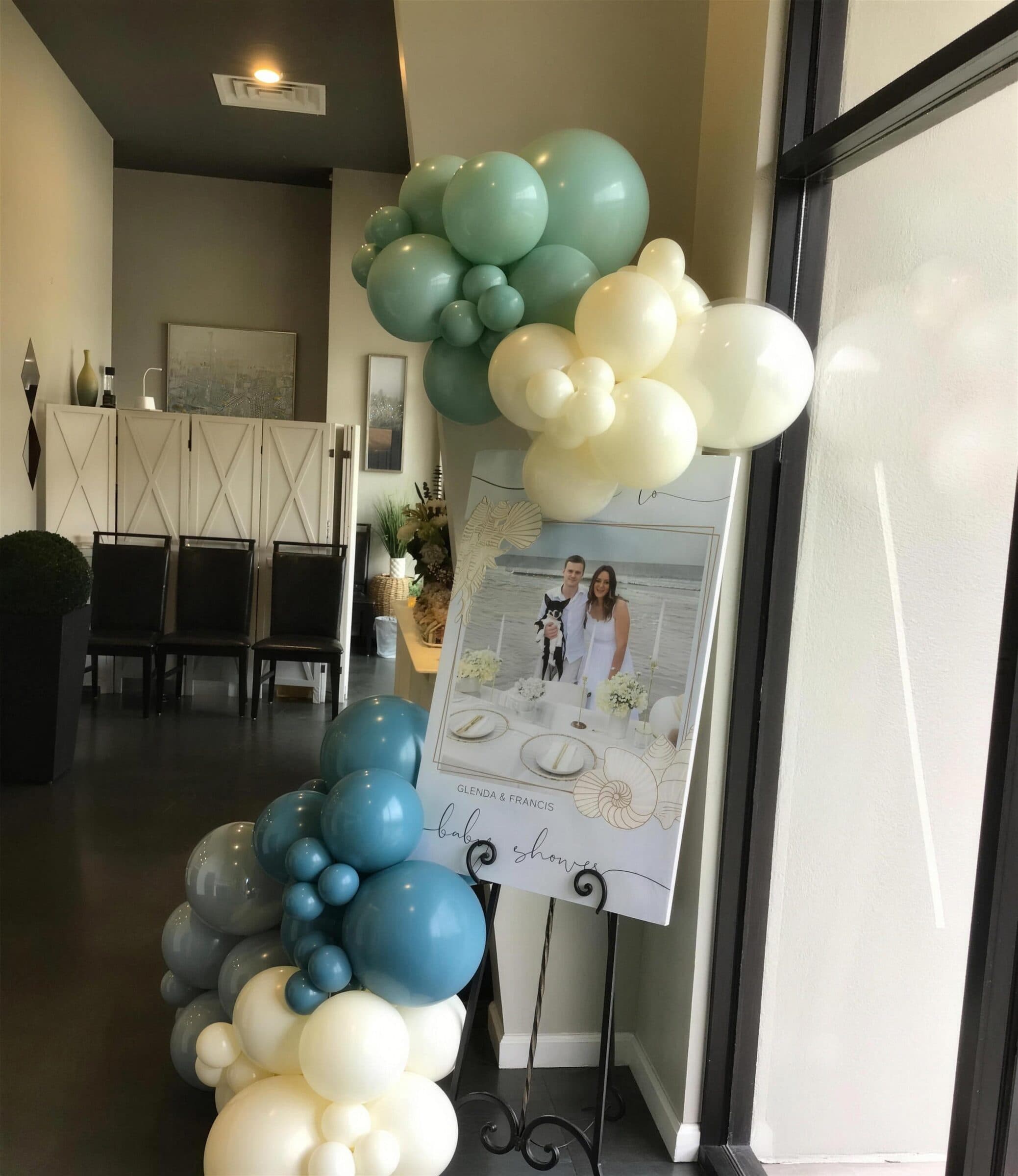 Closer view of the same baby shower welcome easel beside the front window at The Cove at St. Johns, with sage and ivory balloon clusters above and slate-blue balloons below, St. Johns County FL