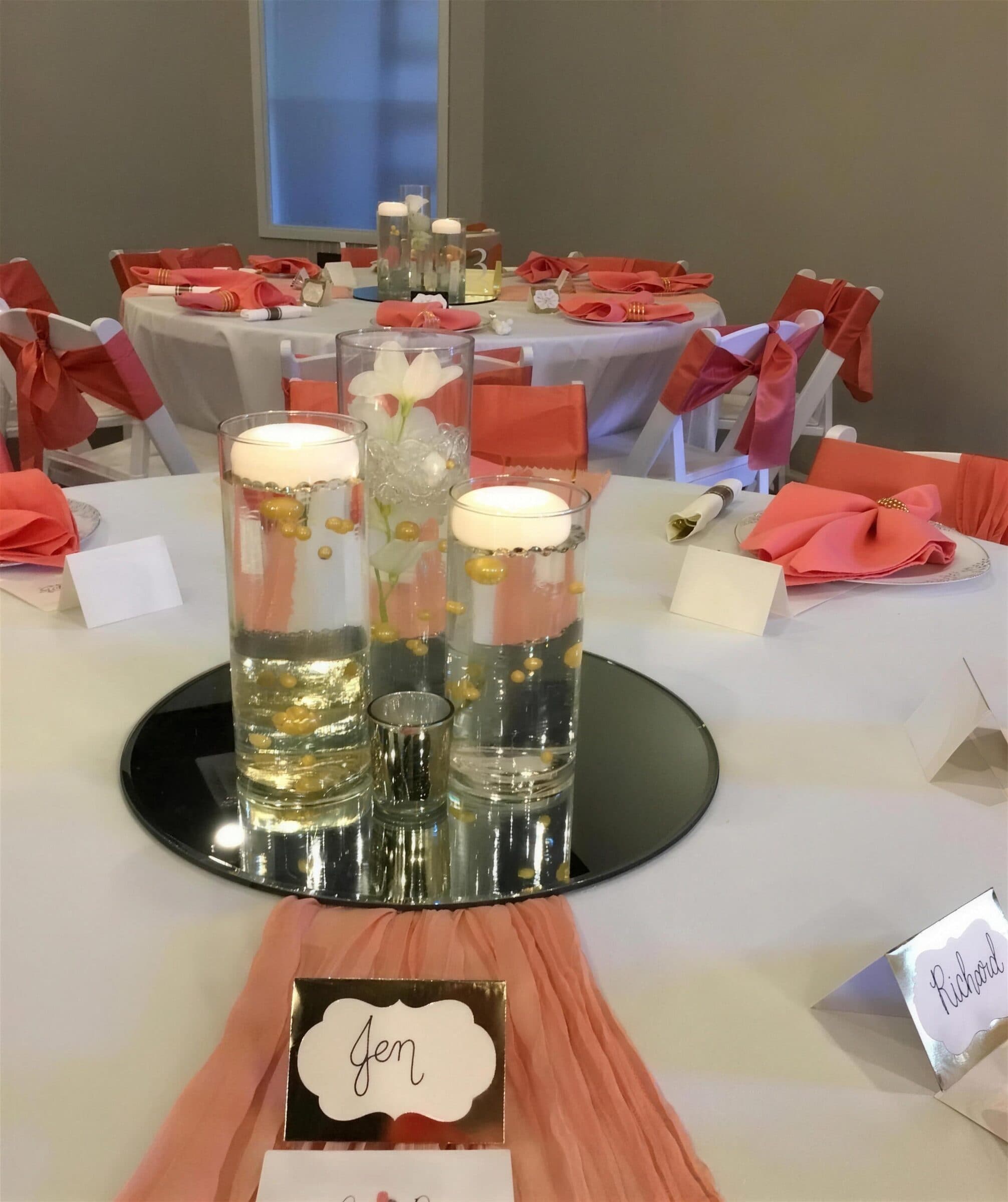 Coral wedding reception tables at The Cove at St. Johns, St. Johns County FL - coral napkins and chair sashes, floating candle cylinders on a mirror round and handwritten place cards