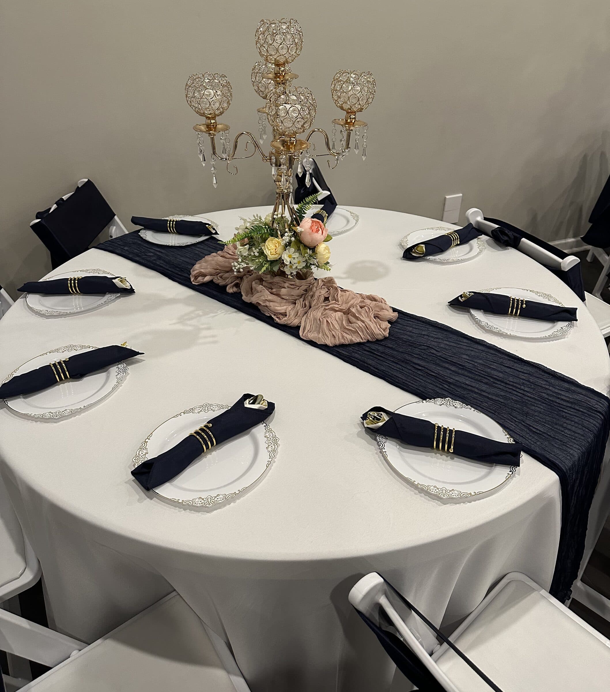 Round guest table with a navy runner, dusty-rose cheesecloth, crystal-globe gold candelabra and navy napkins in gold rings on scalloped chargers at The Cove at St. Johns, near Jacksonville, FL