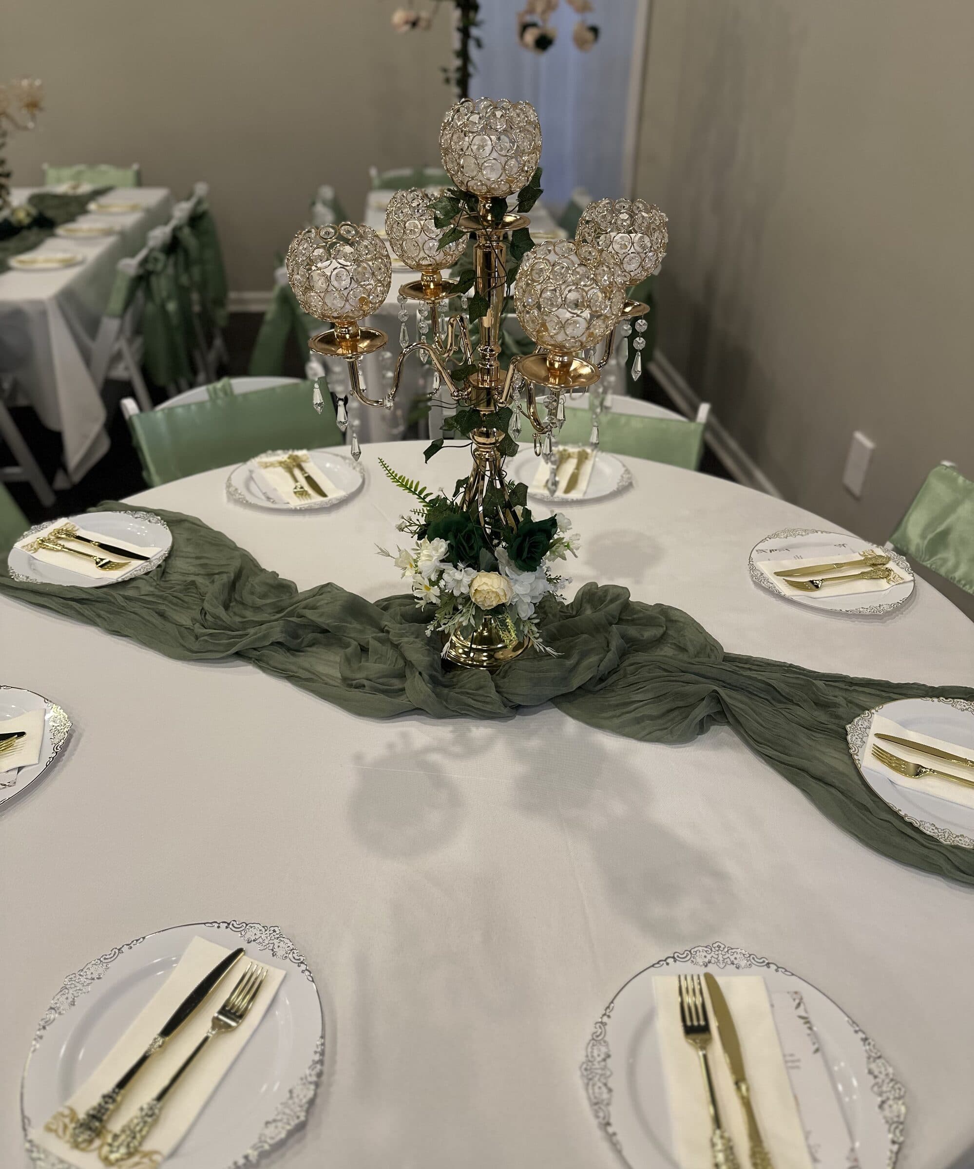 Olive cheesecloth runner pooled around a gold crystal candelabra with white roses and ivy, silver-rim chargers and sage satin chair ties at The Cove at St. Johns, Fruit Cove, St. Johns County FL