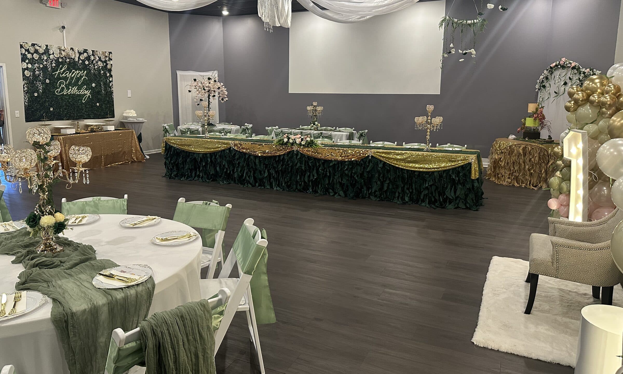 First birthday setup at The Cove at St. Johns - a Happy Birthday greenery wall, emerald ruffled head table with gold sequin swags, lit marquee number one and gold and blush balloons, near Jacksonville, FL