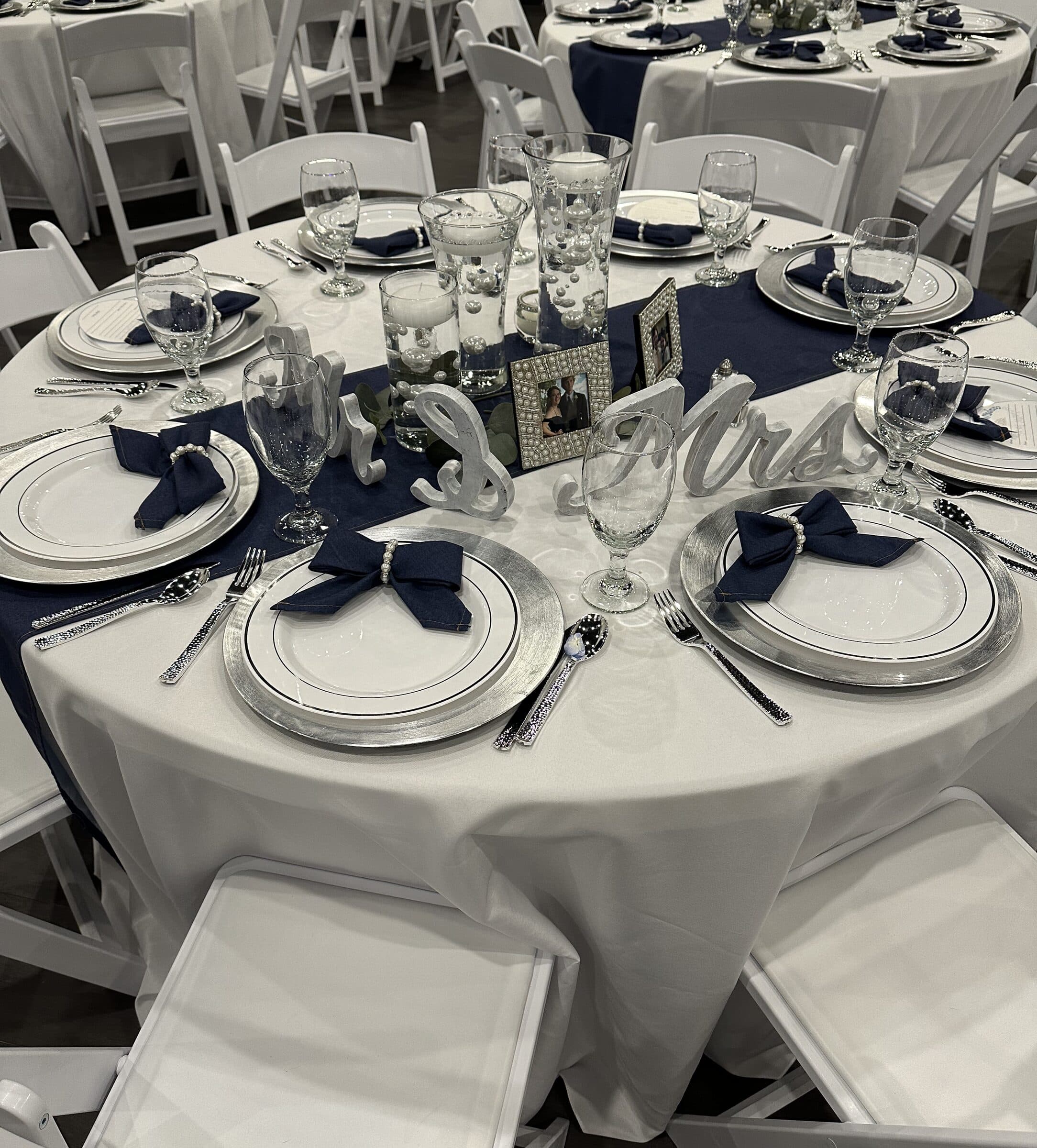 Guest table close-up with navy bow napkins on silver chargers, pearl photo frames and white Mr & Mrs script letters along the navy runner at The Cove at St. Johns, near Jacksonville, FL