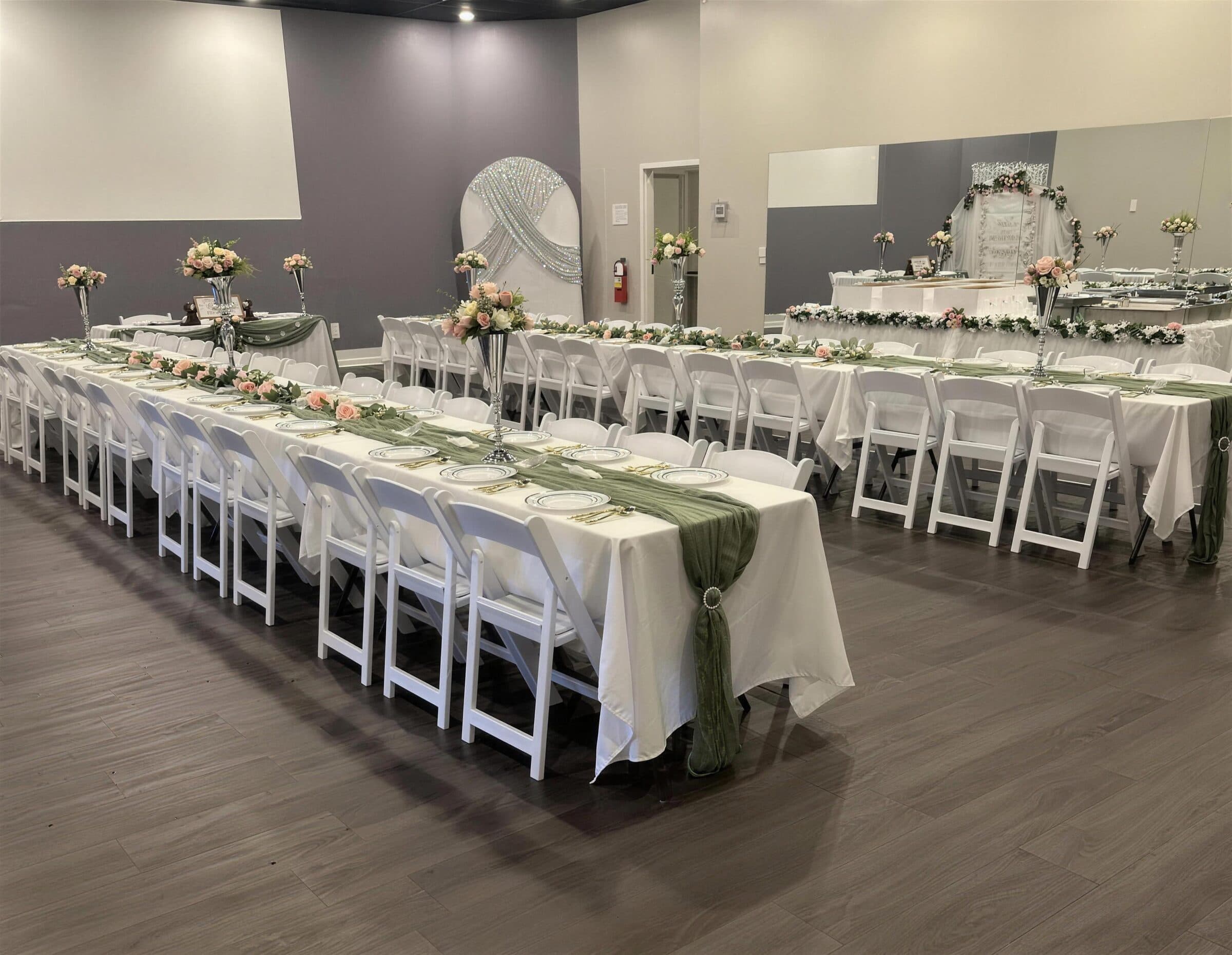 Long banquet rows dressed in white with sage cheesecloth runners, blush rose garlands and tall silver trumpet vases facing a beaded oval backdrop at The Cove at St. Johns, Fruit Cove, St. Johns County FL