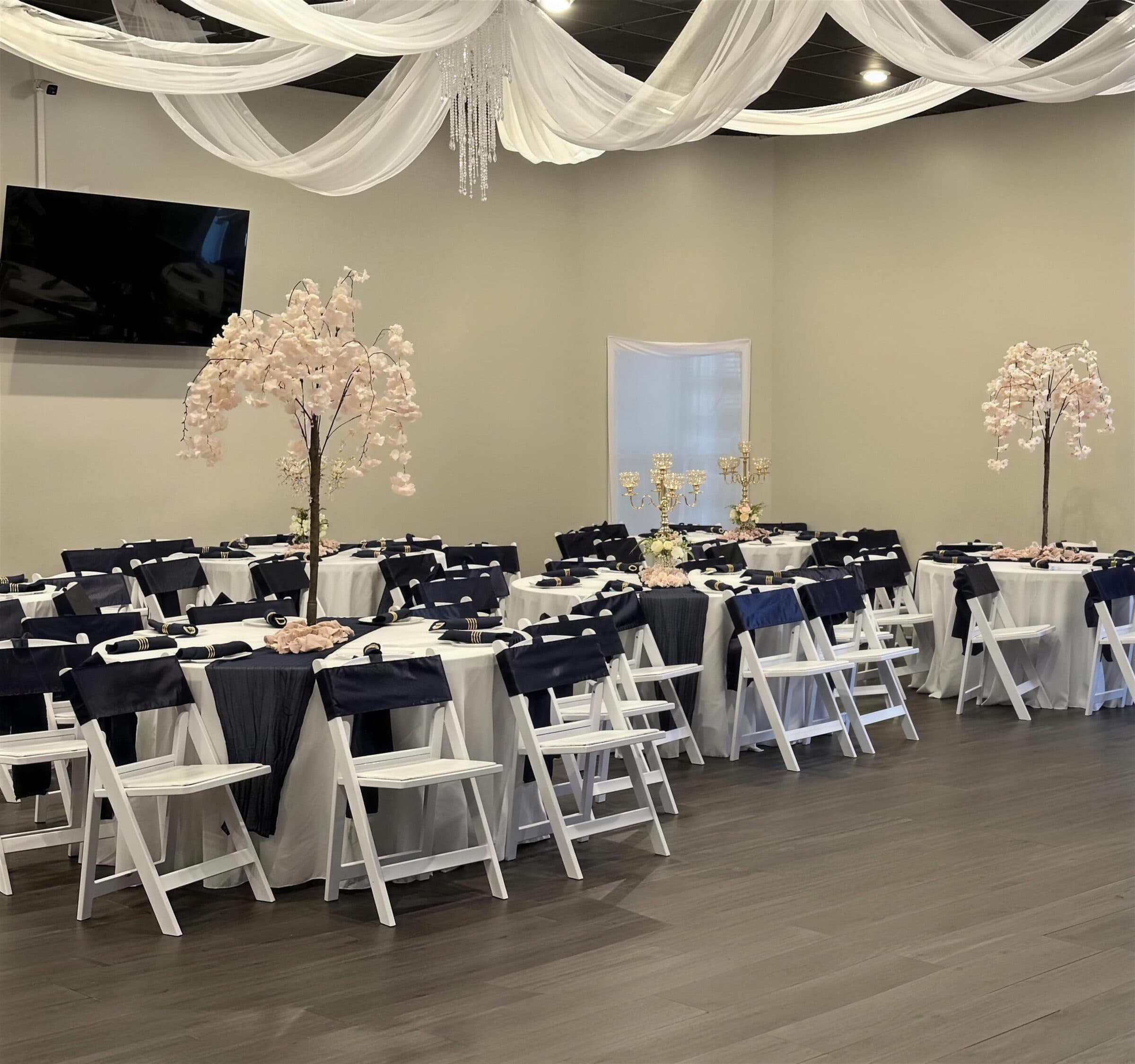 Round tables in navy and blush at The Cove at St. Johns, Fruit Cove FL - navy chair sashes and napkins in gold rings, blush blossom trees and gold candelabras under white ceiling drapes