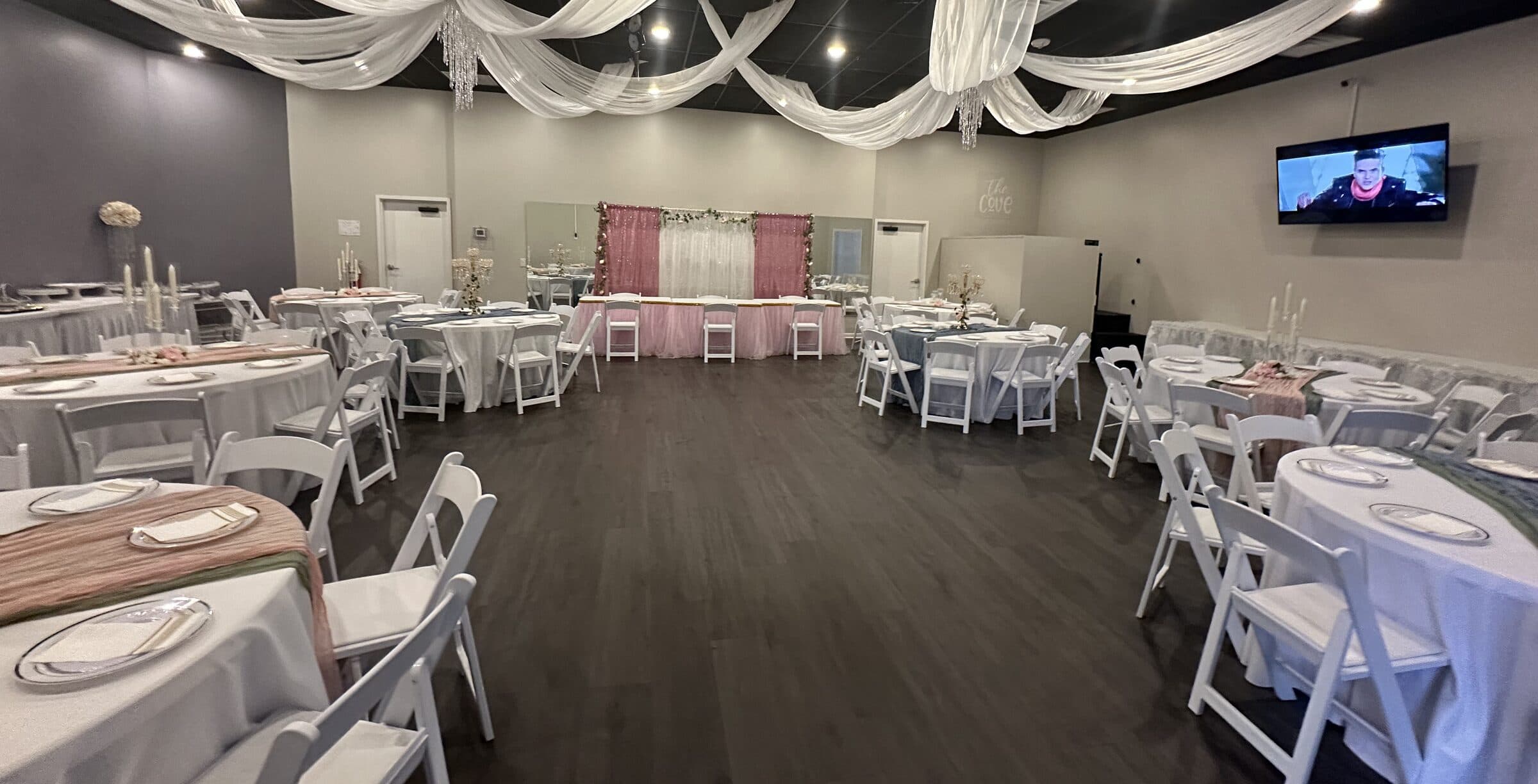 Room set for a reception with white ceiling draping, blush and sage runners, white folding chairs and a blush sequin head-table backdrop at The Cove at St. Johns, St. Johns County FL